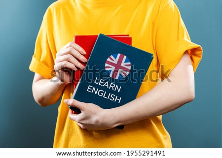 English Language Day. A woman holds English textbooks in her hands. Close-up of books. Blue background. The concept of learning foreign languages. Royalty-Free Stock Photo #1955291491