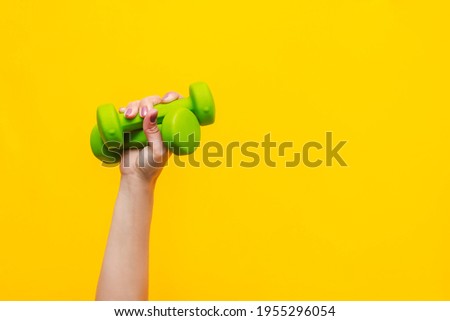 Two green dumbbells in a woman's hand isolated on a bright
color yellow background. Sport equipment. Fitness concept, healthy lifestyle. Copy space for design