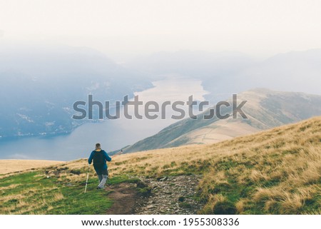 Man is highting with fog misty view mountains and lake landscape. Summer vacations outdoor. Trekking scene on Lake Como alps. Solo tourism, escape, alone traveller. Scenic photo with copy space