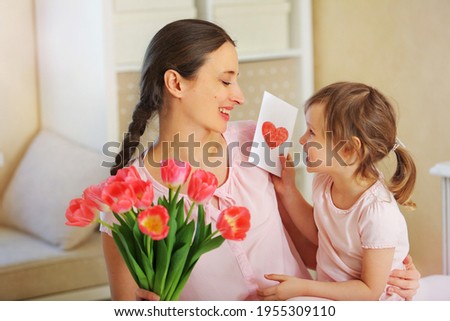 Happy Mother's Day. The child's daughter congratulates her mother and gives her a homemade card and pink tulips flowers. Happy family, relationship with love, enjoying motherhood
