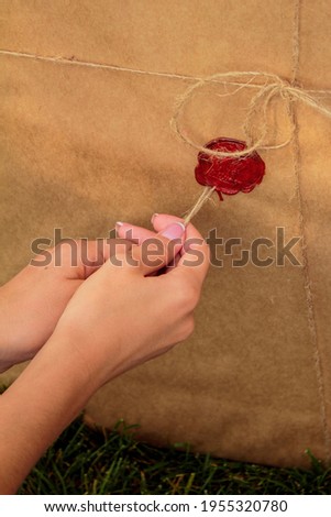 woman opens a gift canvas wrapped in kraft paper and tied in a thin brown rope with twine and sealed with a red seal wax on the grass in the park close-up in warm shades