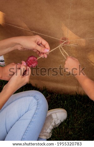 woman opens a gift canvas wrapped in kraft paper and tied in a thin brown rope with twine and sealed with a red seal wax on the grass in the park close-up in warm shades