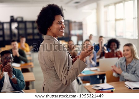 Happy African American professor receives applause from her students while lecturing them in the classroom. Royalty-Free Stock Photo #1955321449