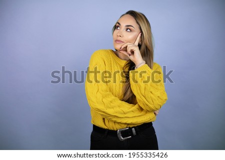 Young beautiful blonde woman with long hair wearing a yellow sweater with serious face thinking about question, very confused idea