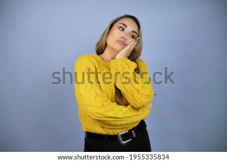 Young beautiful blonde woman with long hair wearing a yellow sweater thinking looking tired and bored with crossed arms