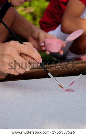 family dad mom children paint with brushes on white canvas a picture by numbers with a simple pencil on the area with numbers in colored acrylic paint outdoors in the park on the grass close-up