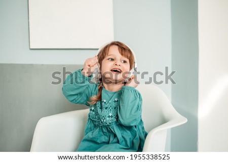 caucasian baby girl in white headphones listens to music and dances in a turquoise blue bright dress.