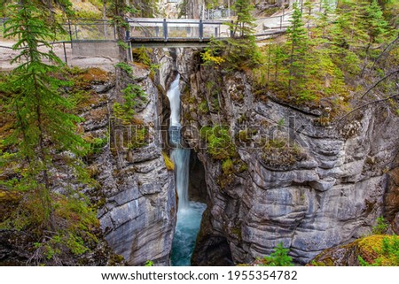 Tourist bridge over a magnificent cascading waterfall in a picturesque gorge Maligne Canyon. Cool cloudy day. Canada. Travel to the Rocky Mountains Royalty-Free Stock Photo #1955354782