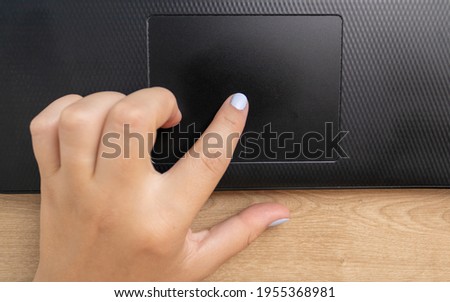 Black keyboard of a handheld photographed diagonally in detail the mouse being used with the finger of a white woman with a modern texture and light blur in the background.