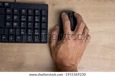 A dark man's hand over a computer mouse with a black keyboard beside a screen message used for work in the home office. Detail of the numeric keys used for calculations.