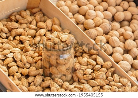 Almonds and walnuts in their shells are sold in the market. The measure of weighing with a glass jar. Close-up, full frame. The concept of harvesting, production and cultivation. Proper nutrition