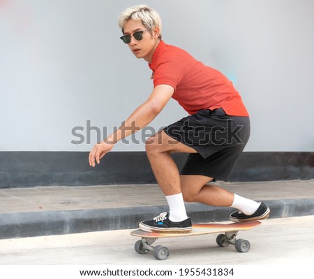 Young asian man riding skateboard on a city street. Portrait of male in t-shirt and black short pants exercise surf skate near sidewalk in urban. Trendy outdoor extreme sport recreation in Asia.  Royalty-Free Stock Photo #1955431834
