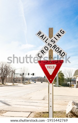 Railway crossing sign beside the road against blue sky, caution signage for driver to stop and yield until safety clear route before drive pass train track. Transportation symbol and regulatory.