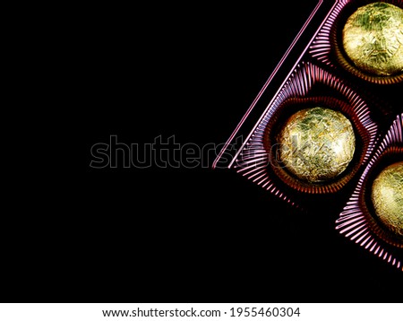A box of chocolates in a golden foil wrapper on a black background. Sweets in shiny foil. Golden color. Sweet dessert. Box of sweets. Sweet food. Black background. Packaging containers.