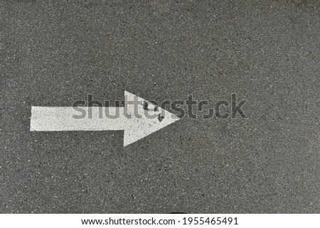 White painted arrow on pavement, weathered and worn white paint. Pointing to the right.