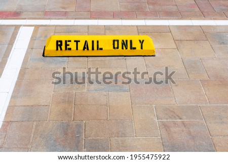 Retail parking only warning sign on yellow concrete wheel stop located on parking stall.