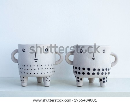 Two empty cute face ceramic plant pots on white wooden shelf isolated on white wall background with copy space. Small modern DIY cement planter trendy decoration.
