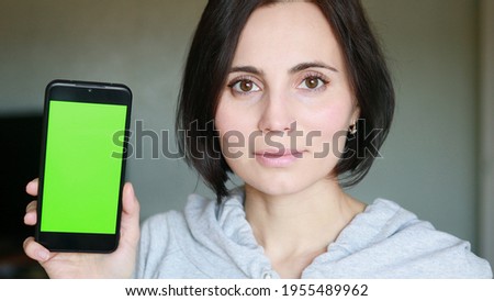 European woman with short hair smiling and showing a mobile phone with green screen 