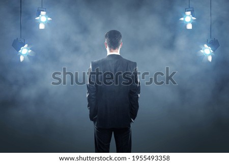 Leadership concept with businessman back on dark stage background with spotlights and smoke
