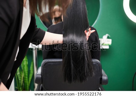 Professional hairdresser making hairstyling for female client in front of mirror. Close-up picture of work process in barber shop. Young brunette woman getting ready for party