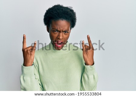 Young african american girl wearing casual clothes shouting with crazy expression doing rock symbol with hands up. music star. heavy concept. 