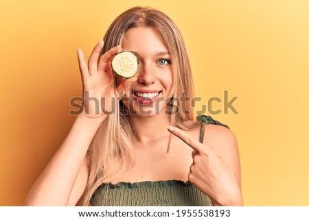 Young beautiful blonde woman holding slicie of cucumber smiling happy pointing with hand and finger 