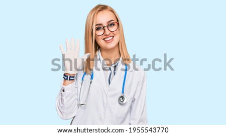Beautiful caucasian woman wearing doctor uniform and stethoscope showing and pointing up with fingers number five while smiling confident and happy. 