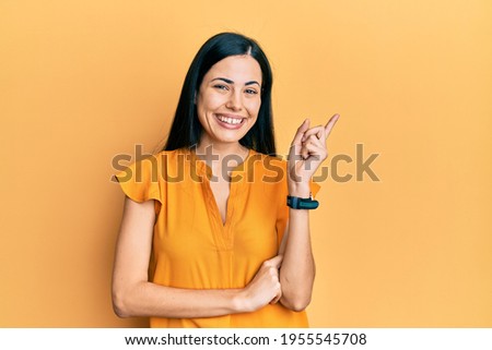 Beautiful young woman wearing casual clothes with a big smile on face, pointing with hand and finger to the side looking at the camera. 