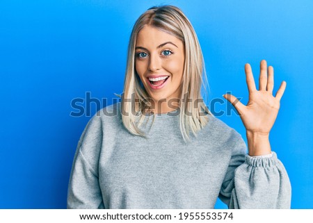 Beautiful blonde woman wearing casual clothes showing and pointing up with fingers number five while smiling confident and happy.  Royalty-Free Stock Photo #1955553574