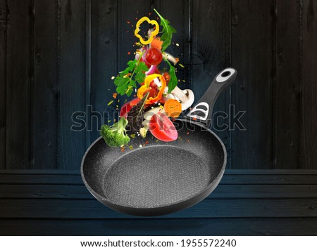 Healthy eating and cooking with various flying chopped vegetables ingredients,wooden table, pan with chicken isolated on black background, front view. Concept diet and healthy eating