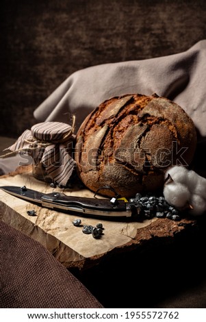 The knife lies on a wooden stump next to a bread and a jar of drying on a dark background