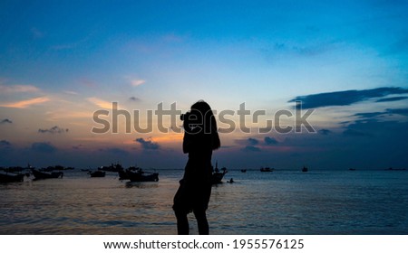 Back view silhouette young girl asian with happy and peacful taking photo on the beach at sunset. Beautiful blonde woman with long hair relaxing at the ocean. Concept of happy, peaceful, relax