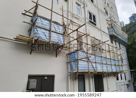Building wrapped in traditional Chinese scaffolding made of bamboo for worker to repair or replace air conditioner above window outside high rise or the entire building in Hong Kong