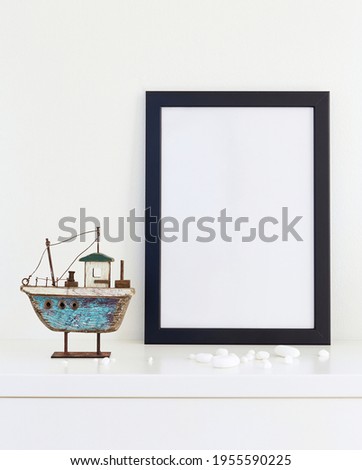 Black mock up picture frame on white shelf with wooden fishing boat against white wall; portrait orientation; stylish interior bright background