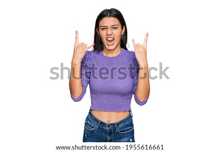 Young hispanic girl wearing casual clothes shouting with crazy expression doing rock symbol with hands up. music star. heavy concept. 