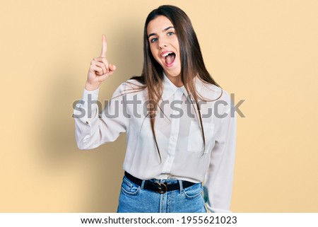 Young brunette teenager wearing business white shirt pointing finger up with successful idea. exited and happy. number one. 