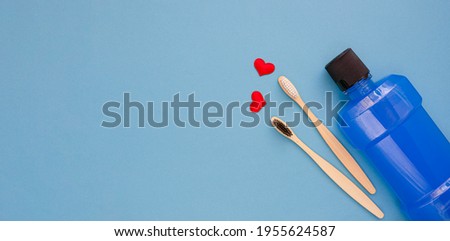 Mouthwash, two wooden bamboo toothbrushes and several red hearts on a blue background. Oral and gum care concept. Brushing your teeth with love, taking care of your teeth. top view, copy space, Banner