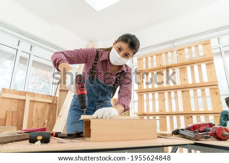 Selective Focus, A Confident female carpenter uses a hand drill to assemble the wood in the carpentry shop. Asian handywoman apprentice working in a workshop. DIY woodworking crafts and Hobby concepts
