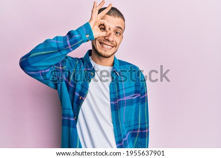 Hispanic young man wearing casual clothes smiling happy doing ok sign with hand on eye looking through fingers 
