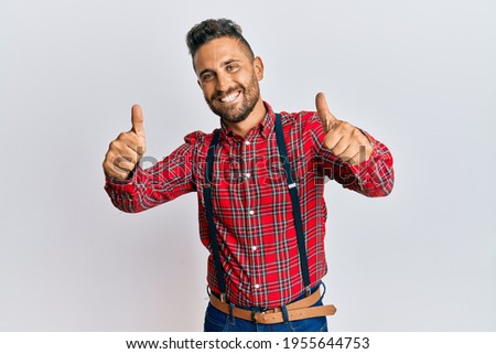 Handsome man with beard wearing hipster elegant look approving doing positive gesture with hand, thumbs up smiling and happy for success. winner gesture. 
