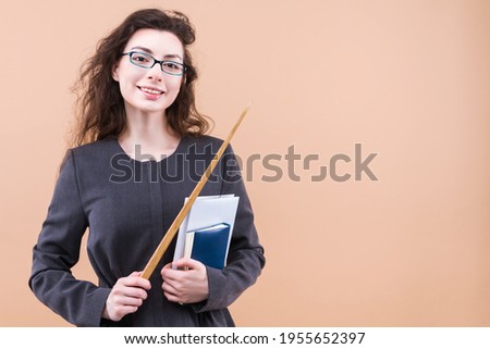 Photo portrait of teacher keeping pointer smiling holding book isolated on pastel beige color background. Young curly woman lecturer in casual jacket is ready to teach students. Study at university 