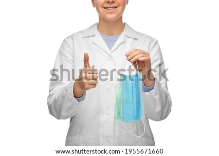 healthcare, medicine and pandemic concept - close up of smiling female doctor or scientist holding two face protective medical masks showing thumbs up gesture over white background
