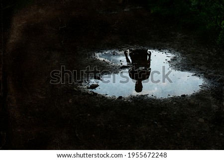 A dark, atmospheric edit of a mysterious man silhouetted in a puddle.. With a grunge, vintage edit.