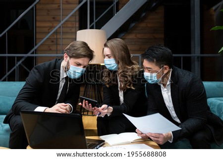 Group of men and woman hold business meeting, near laptop, wearing protective medical masks on face, in conference room, business meeting