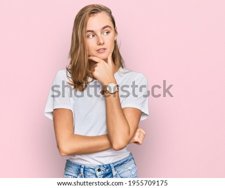 Beautiful young blonde woman wearing casual white t shirt with hand on chin thinking about question, pensive expression. smiling with thoughtful face. doubt concept. 