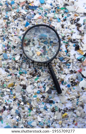 Stock photo of microplastics scattered on a white surface with a magnifying glass in the center