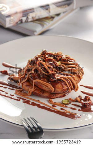 Brown Pancake with chocolate and caramel sauces and nuts in the top, on white background 