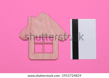 The concept of buying and paying rent for housing. Mini house and credit card on pink background. Top view