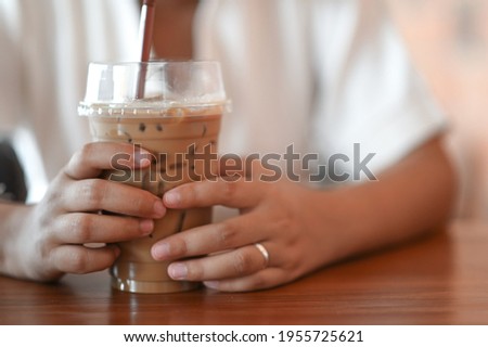 A woman grabbing iced coffee with both hands in the coffee shop. Royalty-Free Stock Photo #1955725621