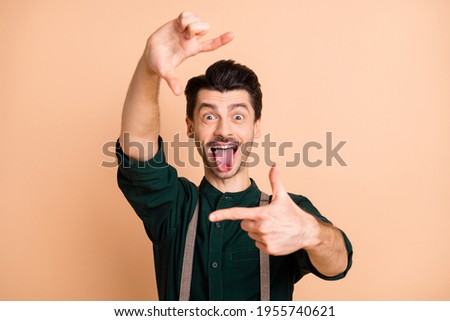 Photo of cheerful funky young woman hold fingers make frame stick out tongue isolated on pastel beige color background